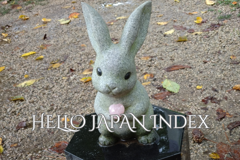 A small stone rabbit statue holding a pink heart, photographed outdoors on gravel, used as the cover image for the HELLO JAPAN Index.