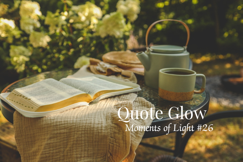 An open book, a teapot, and a cup of tea resting on a garden table surrounded by soft white flowers and warm sunlight. The image features the title "Quote Glow – Moments of Light #26."