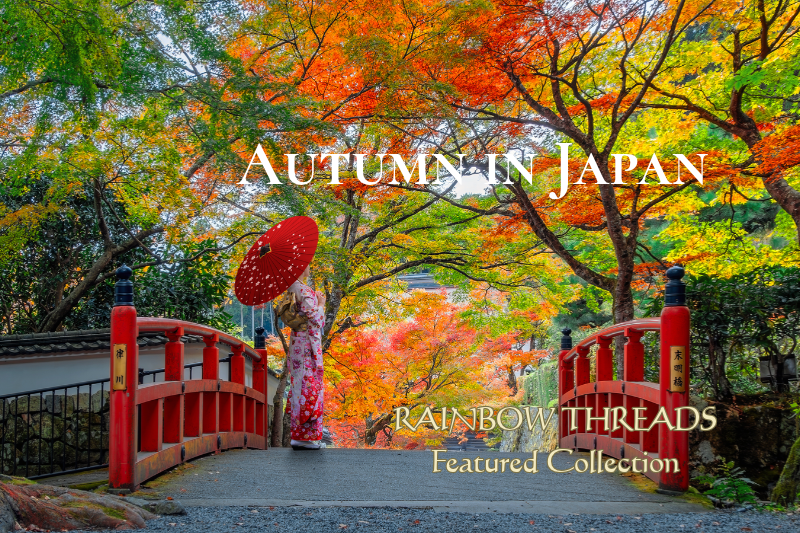 Autumn in Japan — Rainbow Threads Featured Collection. A woman holding a red Japanese parasol stands on a traditional red bridge, surrounded by vibrant autumn maple leaves in shades of red, orange, yellow, and green.